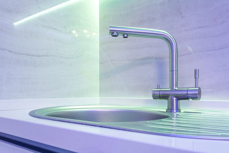 Modern three-way kitchen faucet mounted beside a stainless steel sink for separate filtered water access.