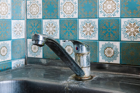 Mineral buildup and corrosion cover a kitchen faucet and sink affected by hard water.