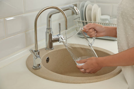 Water flows from a secondary drinking water faucet into a clear pitcher beside the main faucet