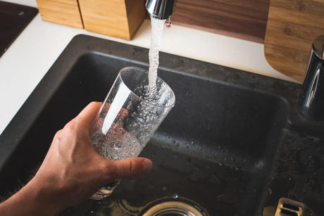 Hand holds a clear glass under dedicated RO faucet to collect fresh mineral-rich filtered water from alkaline and remineralization reverse osmosis units.