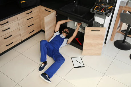 Professional plumber lies under kitchen sink to perform alkaline water filter cartridge replacement and pipeline maintenance work.