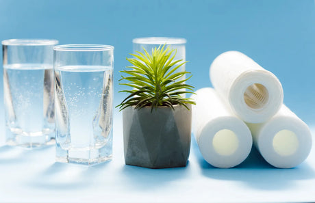 Clear tumblers of purified water stack alongside spare PP filter cartridges, displaying consumable parts for routine upkeep of remineralizing under-sink reverse osmosis hardware.