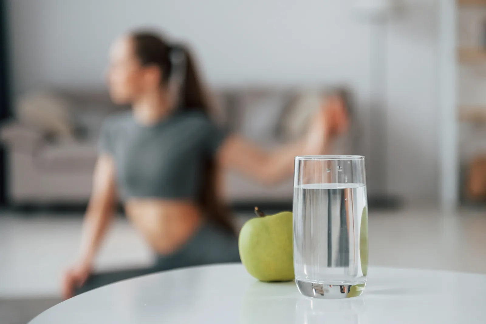 Glass of filtered water with a green apple next to a woman doing yoga, showcasing kidney-friendly hydration for active lifestyles.