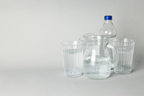 Glass pitcher, drinking glasses, and a bottled water container, showing tap/filtered vs bottled water presentation