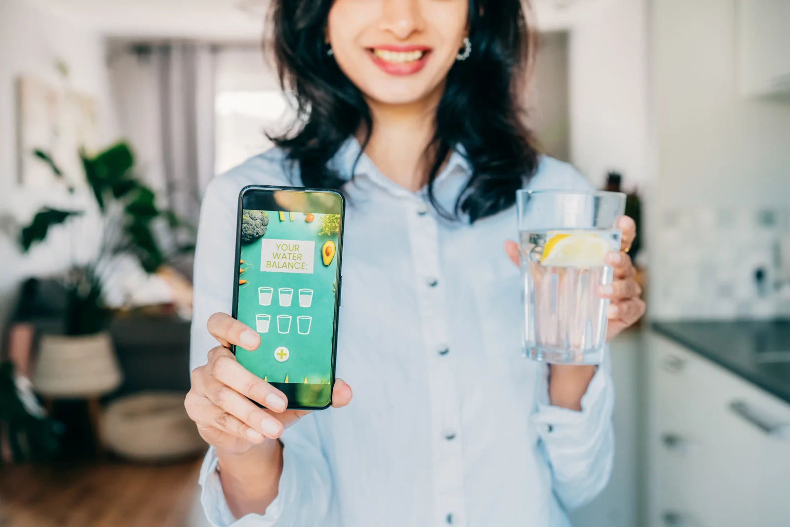 Holding a smartphone with a water balance app and a glass of water, tracking daily hydration and consumption