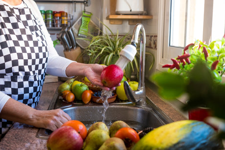 Person washing a red apple under running water from a kitchen faucet with a filter attachment