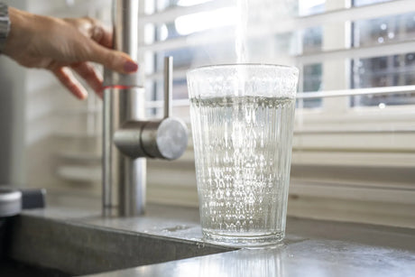 A person fills a glass with tap water, a potential source of fecal coliform contamination.