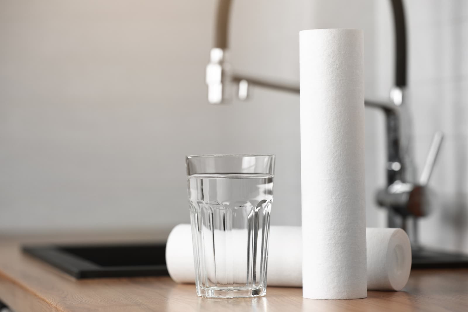 Glass of clean water beside replacement filter cartridges on a kitchen countertop.