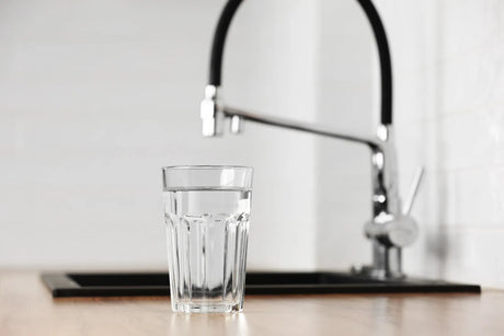 Clear glass of tap water at kitchen sink, illustrating source of pharmaceutical-contaminated drinking water.