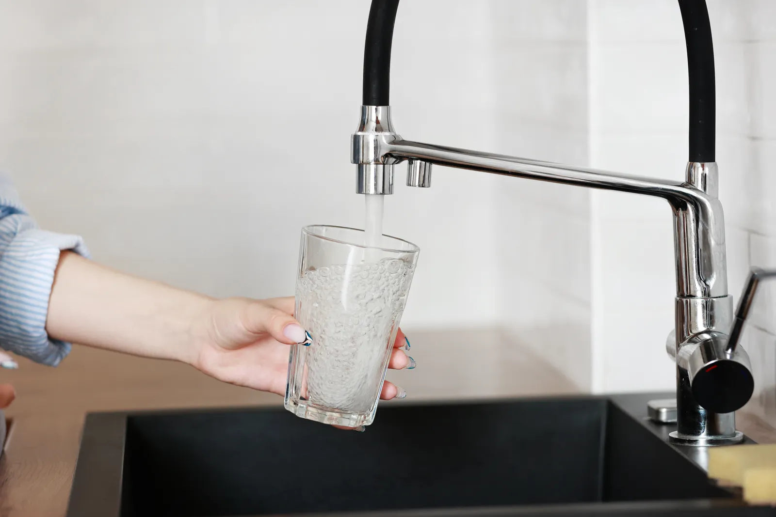 Clear glass filling with clean water from modern kitchen faucet, representing safe drinking water solution for high TDS levels