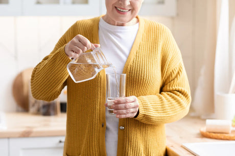 An elderly woman pours low-sodium water into a glass, supporting senior health.