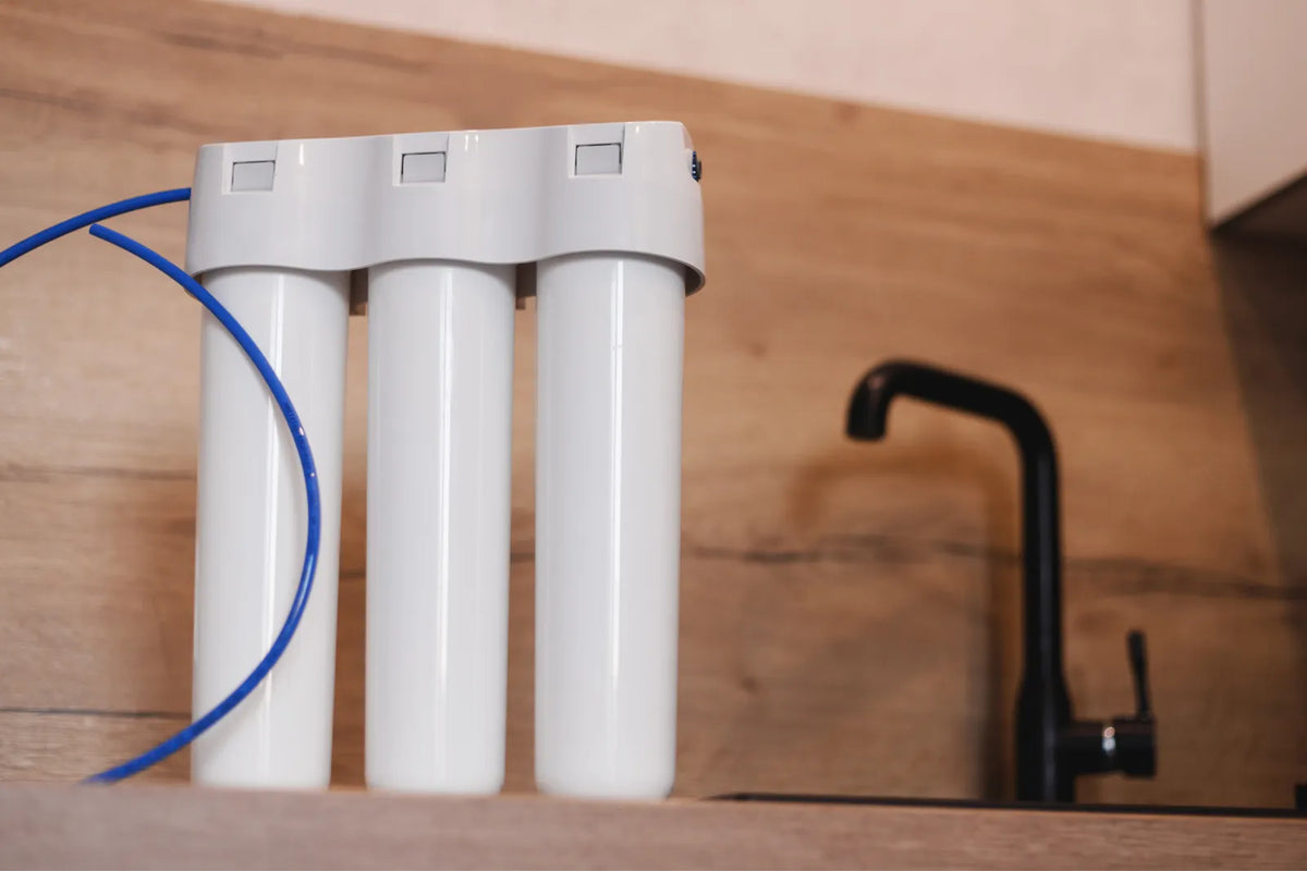 Three-stage under-sink water filter system with white cartridges, used for multi-level water purification and maintaining consistent water flow.