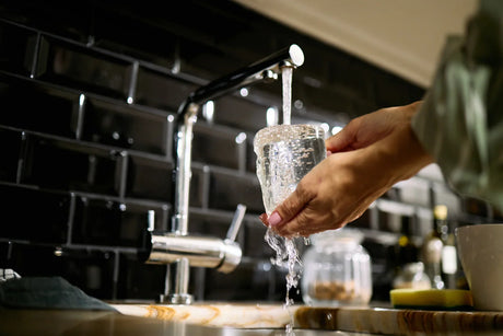 Pouring NSF-certified filtered water into a glass at a modern kitchen sink, ensuring safe drinking water.