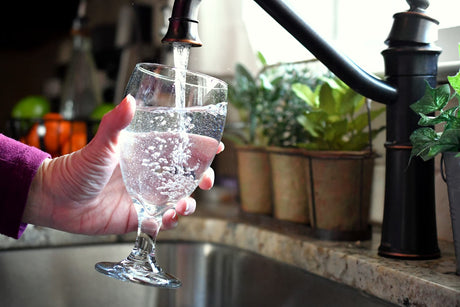 Clear drinking water filling a glass from a kitchen faucet over the sink.