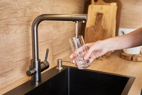 Woman filling a clear drinking glass with water from a kitchen faucet over the sink