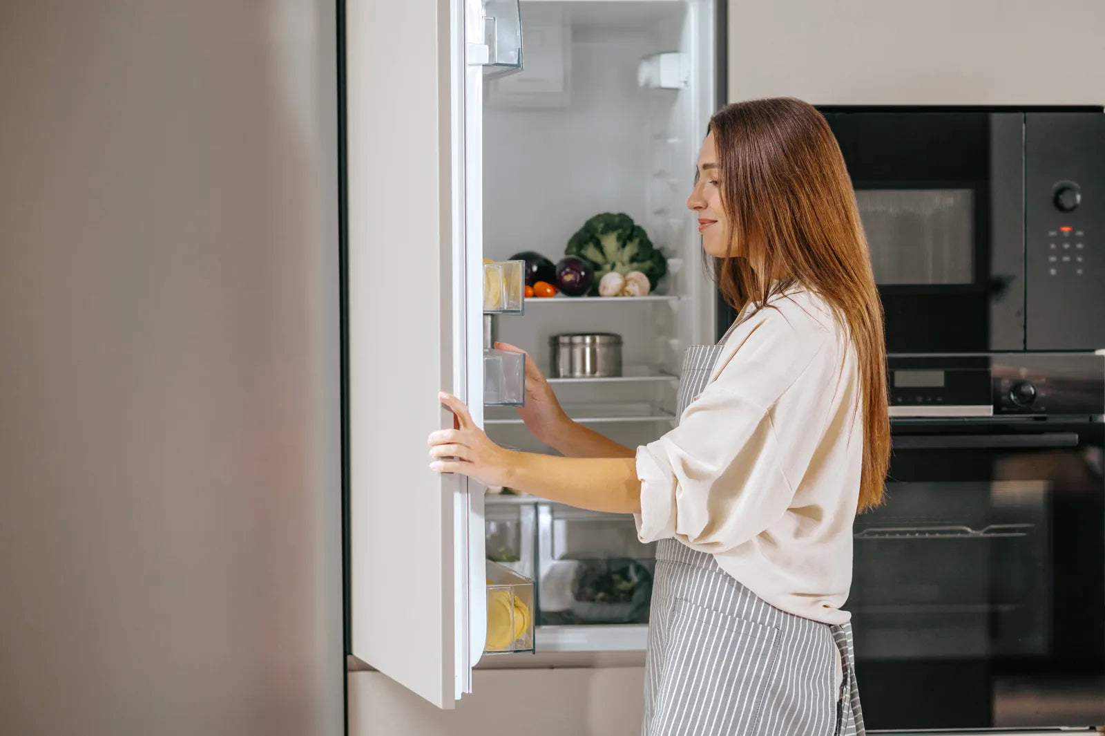 Woman opening a well-stocked refrigerator, illustrating the location of the water filter compartment for replacement.