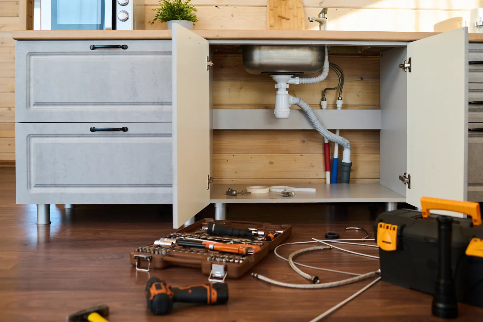 Tools and parts laid out under an open kitchen sink for reverse osmosis drain saddle installation.