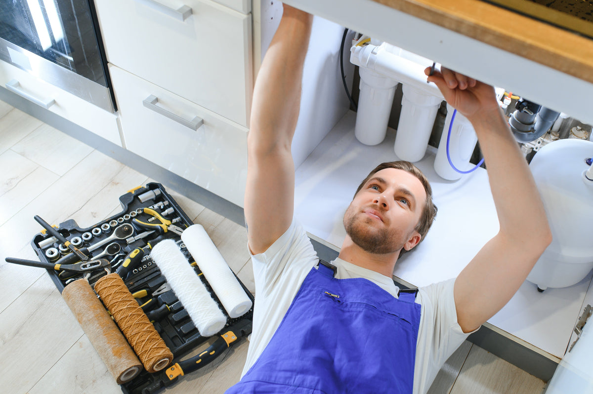 Technician working on an under-sink reverse osmosis system with replacement filter cartridges and tools nearby