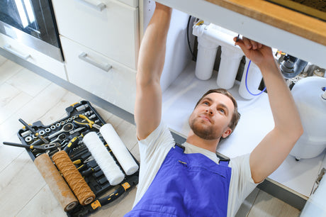 Technician working on an under-sink reverse osmosis system with replacement filter cartridges and tools nearby
