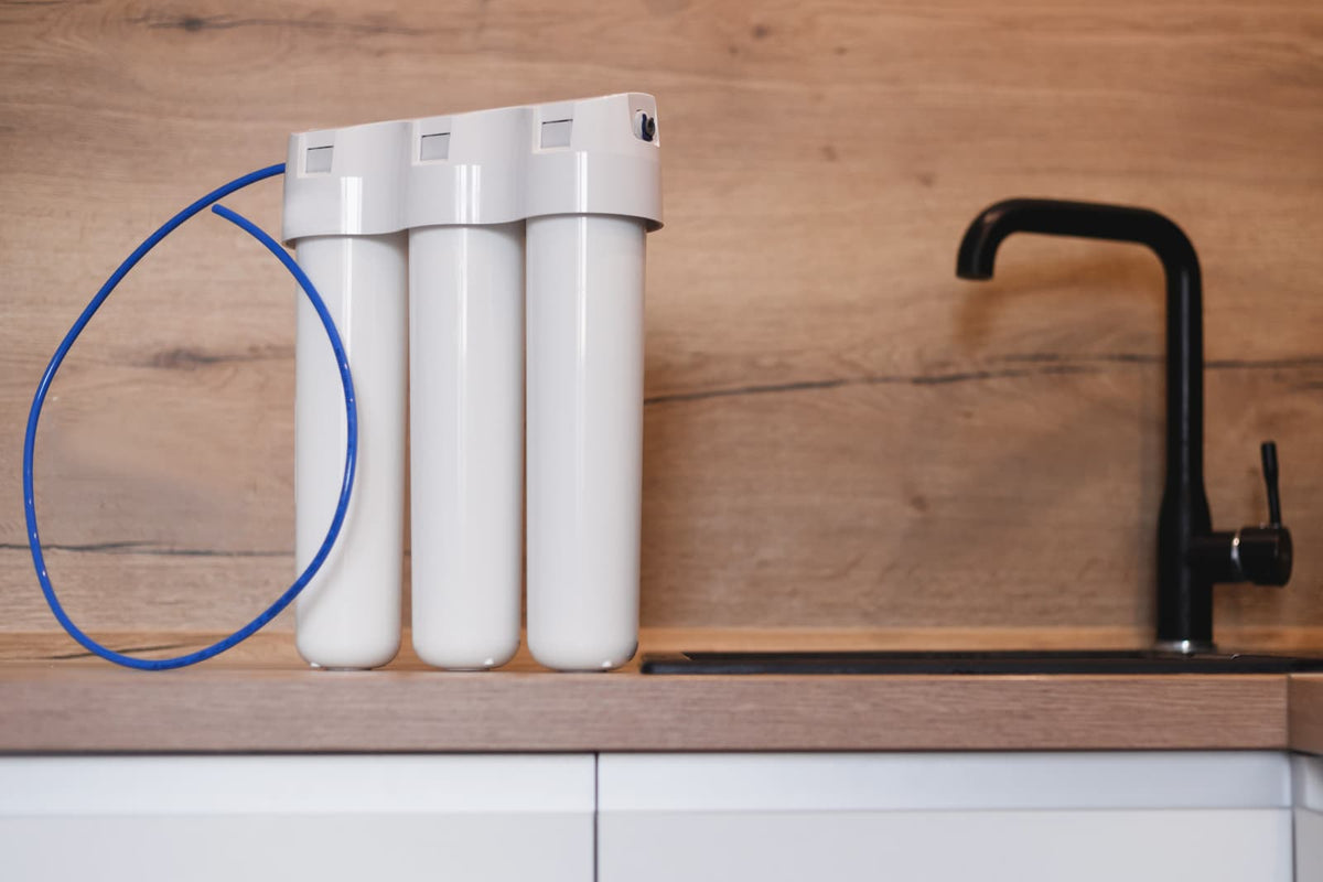 membranes (1).jpg Three-stage water filter housing with blue tubing beside a black kitchen faucet