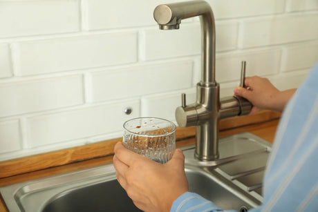 Person turning a kitchen faucet handle to pour filtered water into a clear glass at the sink.