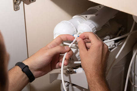 Homeowner checks an under-sink reverse osmosis system for a water leak.