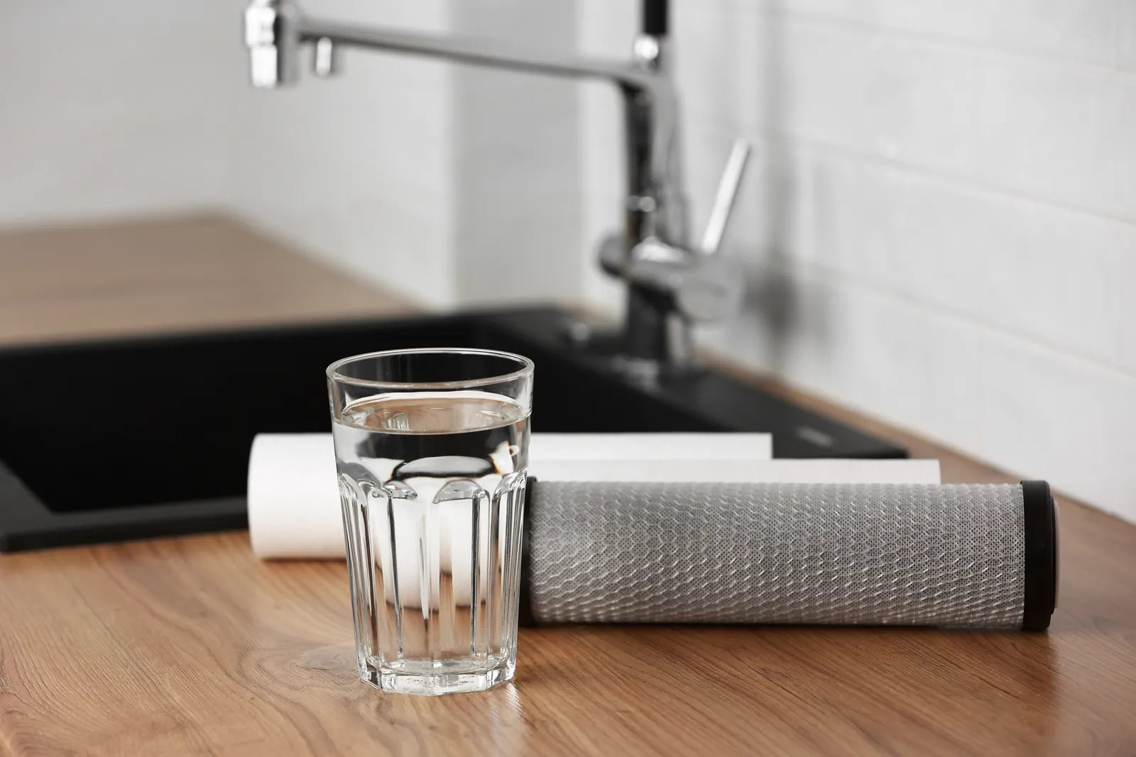 Clean drinking water in a glass next to water purifier cartridges on a kitchen countertop.