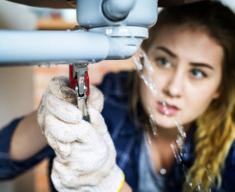 A gloved technician repairing an under-sink water pipe leak to prevent home water damage and restore plumbing functionality