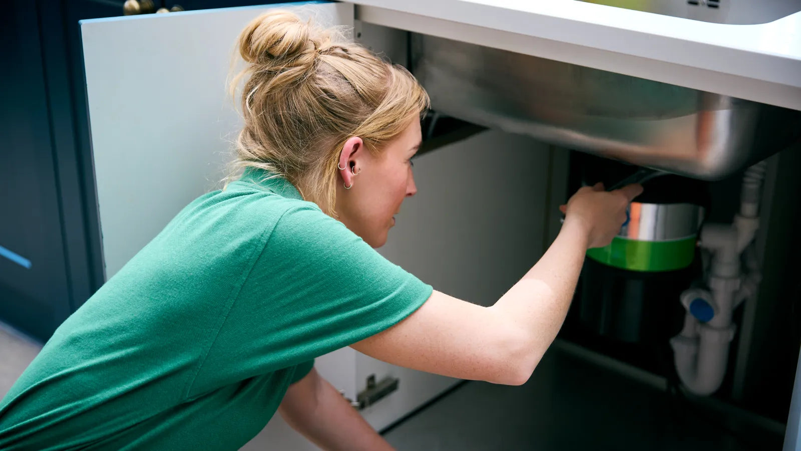 A woman installing a no-drill under-sink water filter next to kitchen drain pipes