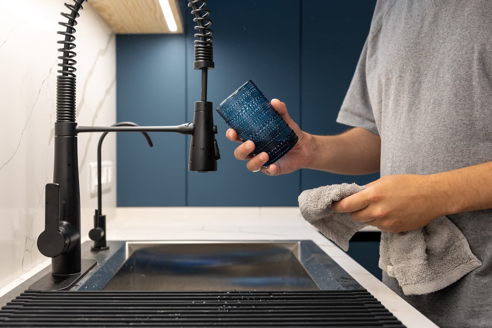 Person holding a blue cylindrical insert beside a black pull-down kitchen faucet and sink.