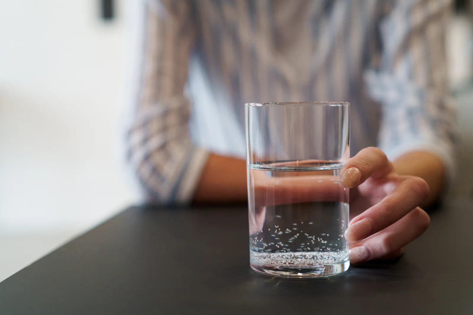 Hand holding a glass of filtered water, showcasing clean, microplastic-free drinking water from a home water filtration system.