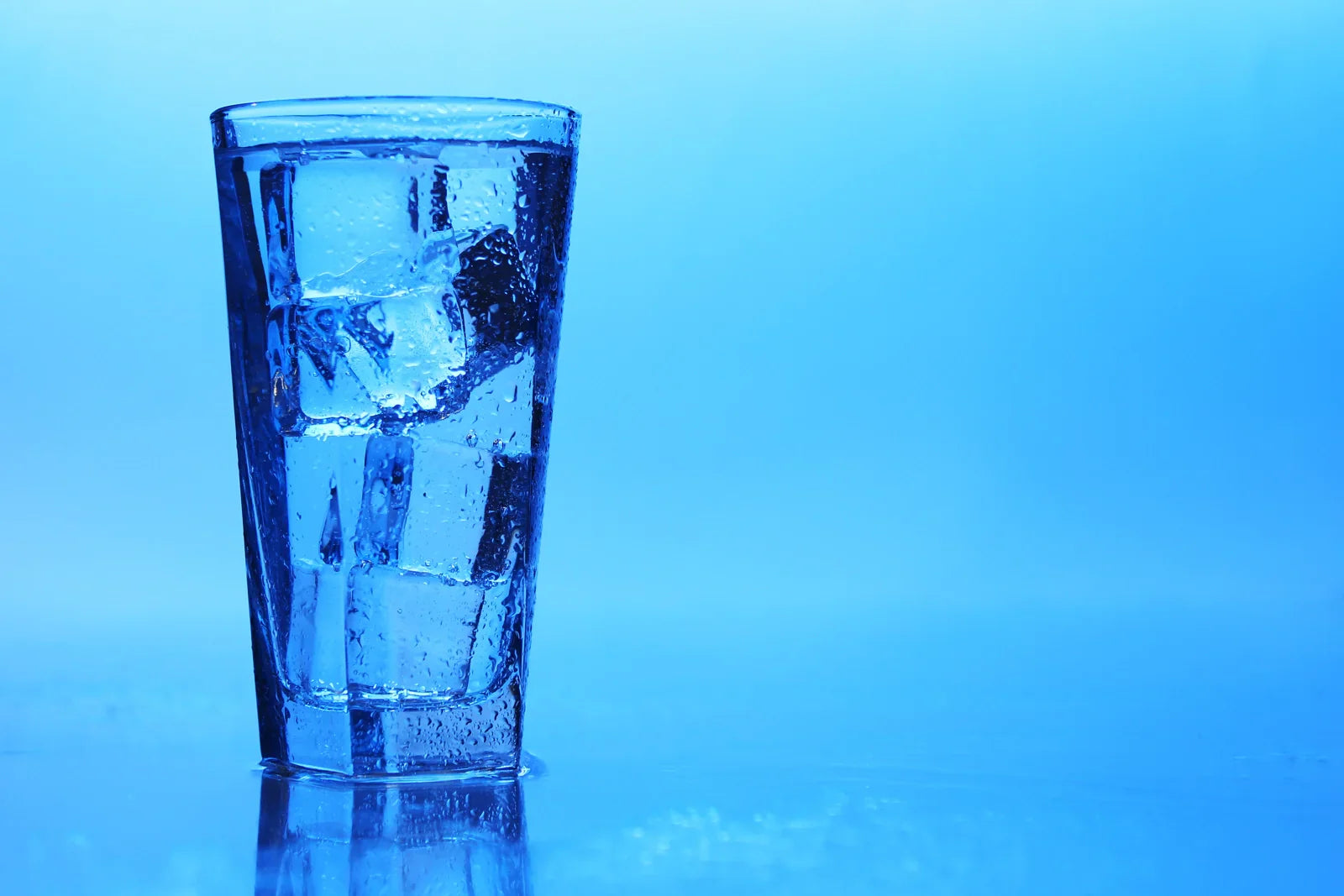 Tall glass filled with ice cubes used in a kitchen setting for serving cold drinking water and beverages