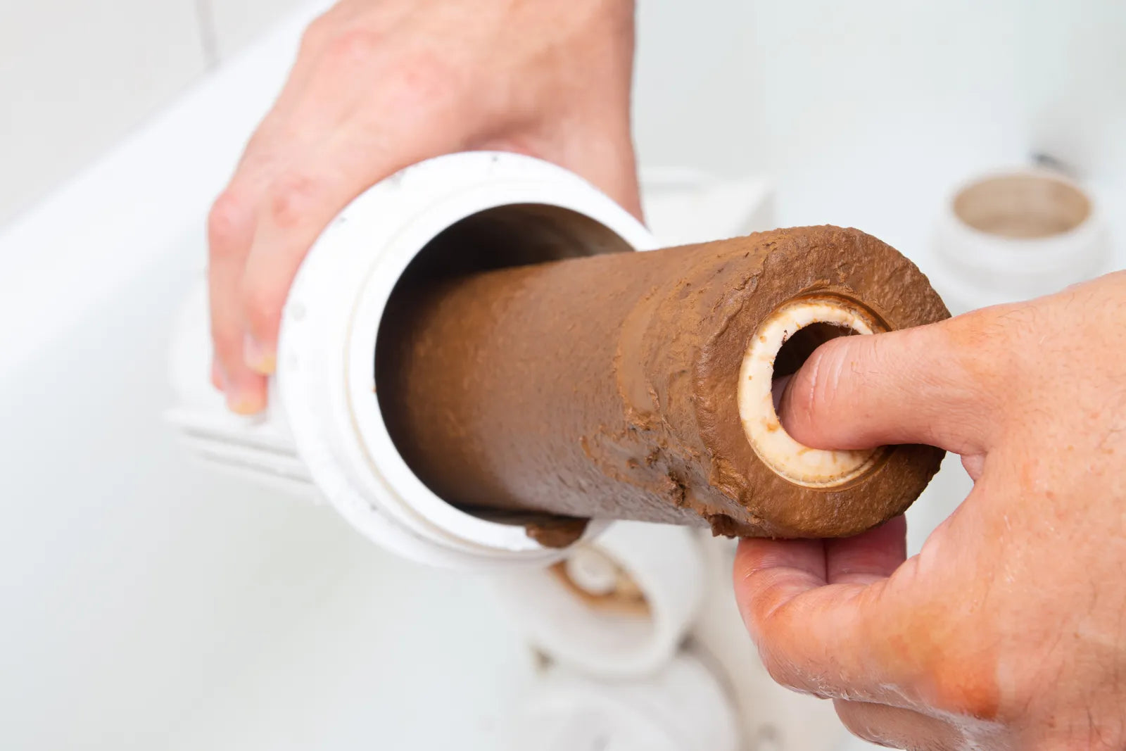A heavily clogged, brown sediment-covered water filter cartridge being removed from its housing