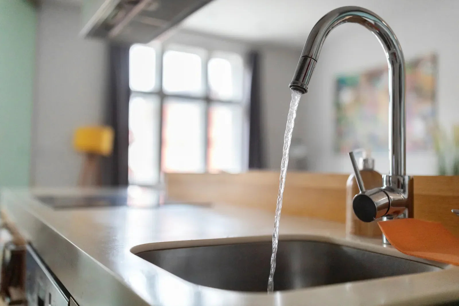 Close-up of kitchen sink faucet with clean water stream, bright home background