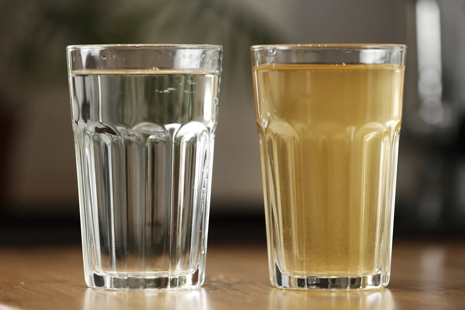 Two glasses of water on a table, one clear and one yellow, showing the visual difference between safe, filtered water and discolored tap water.